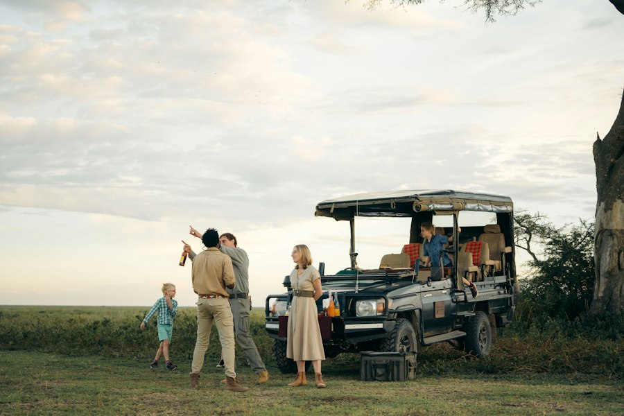 Safari guide chatting with a family beside an open game-drive vehicle