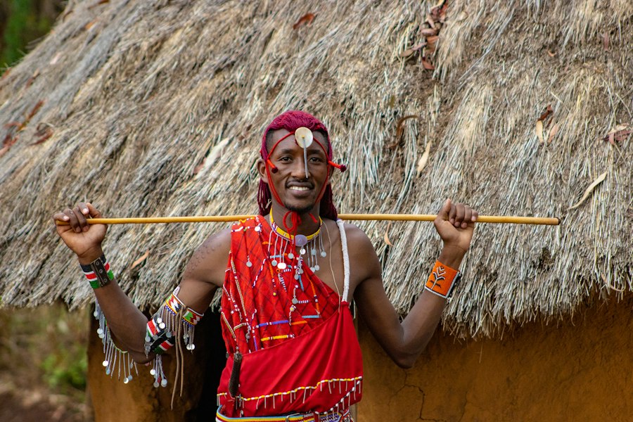 Smiling Maasai host in a red shuka outside a thatched home