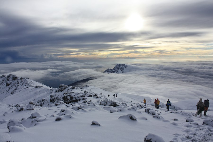 Trekkers crossing snowy slopes near the summit of Kilimanjaro above the clouds