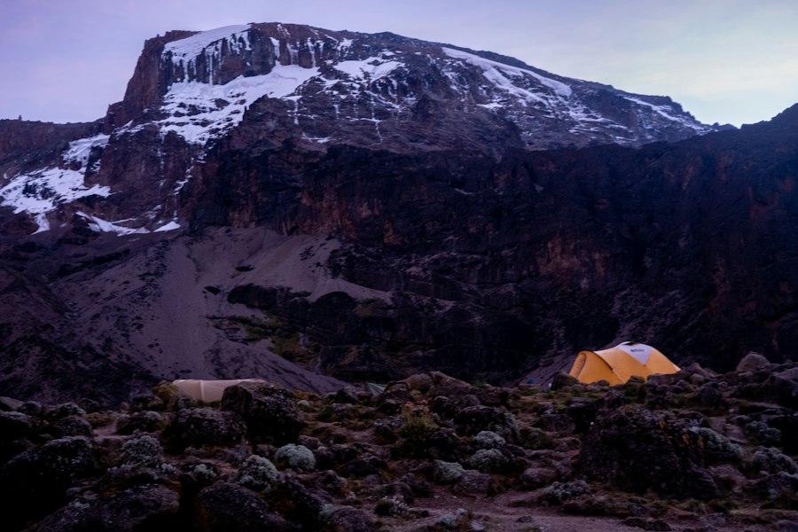 A camp tent on rocky ground below Kilimanjaro’s snowy summit