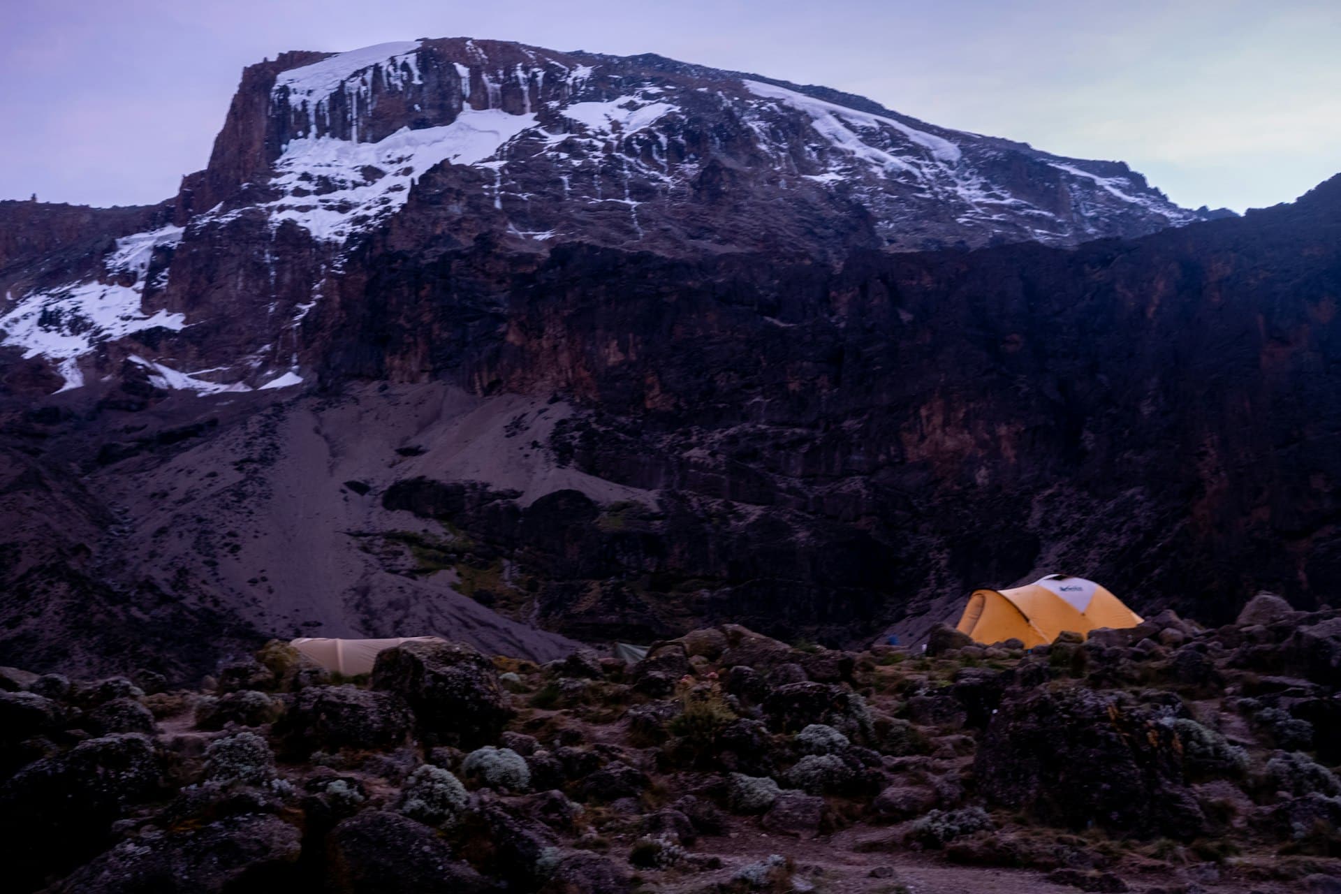 A camp tent on rocky ground below Kilimanjaro’s snowy summit