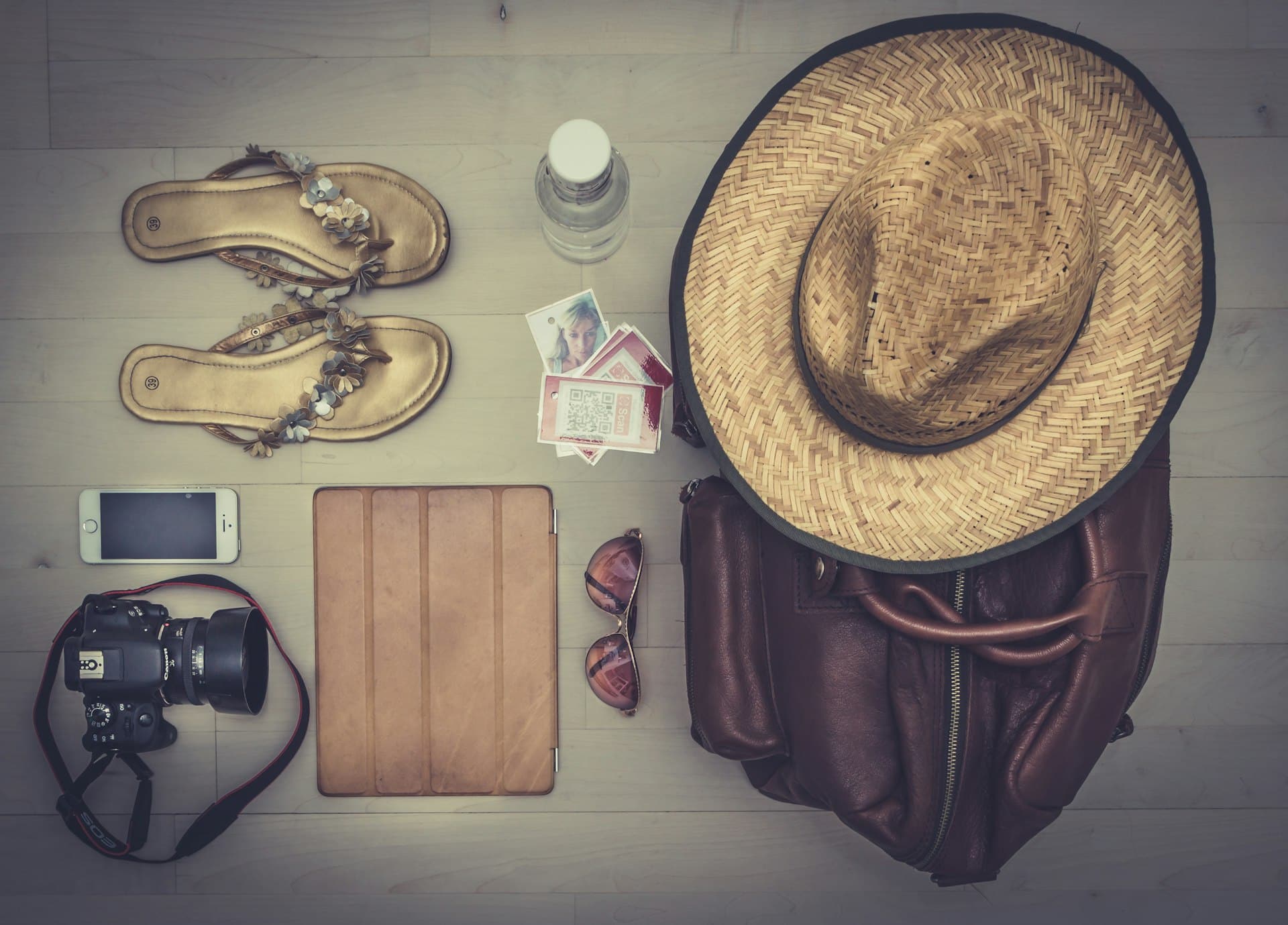 Straw hat, camera, sandals and a leather bag laid out for a trip