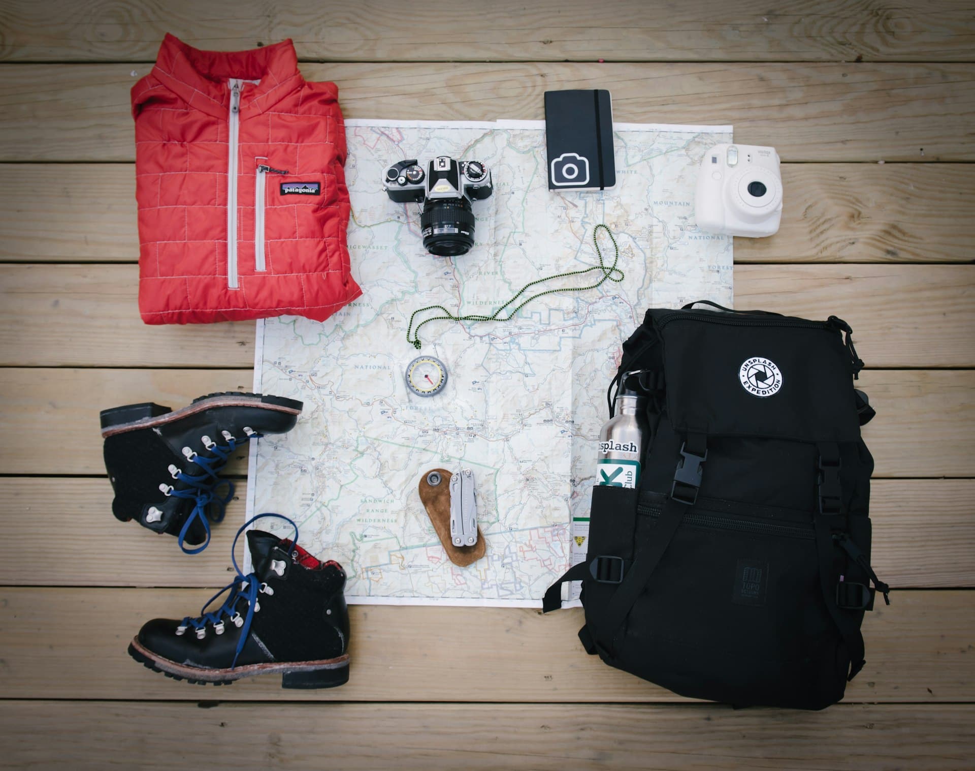 Hiking boots, map, compass, jacket and backpack laid out before a climb