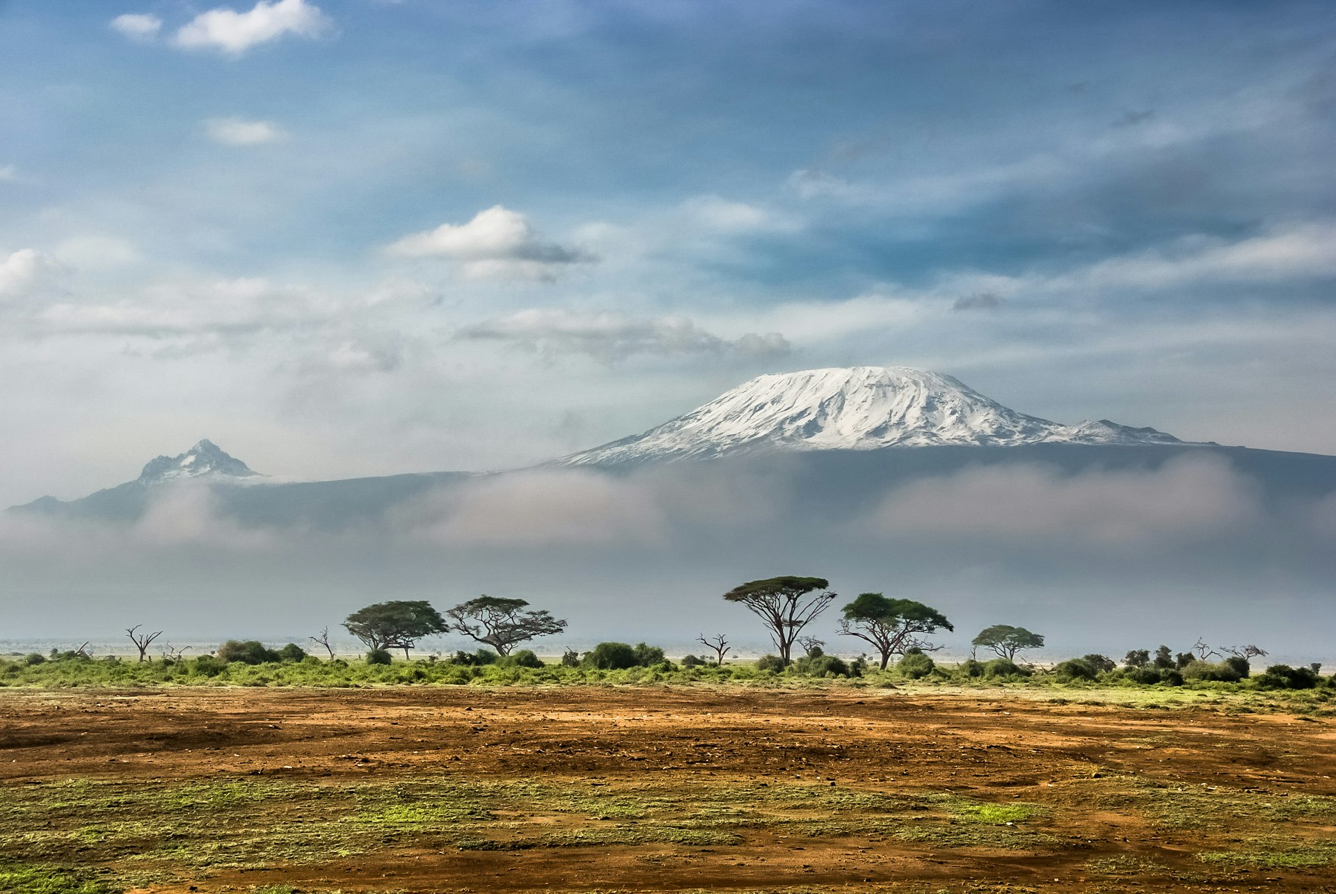 Snow-capped Mount Kilimanjaro rising above a band of cloud and acacia plains